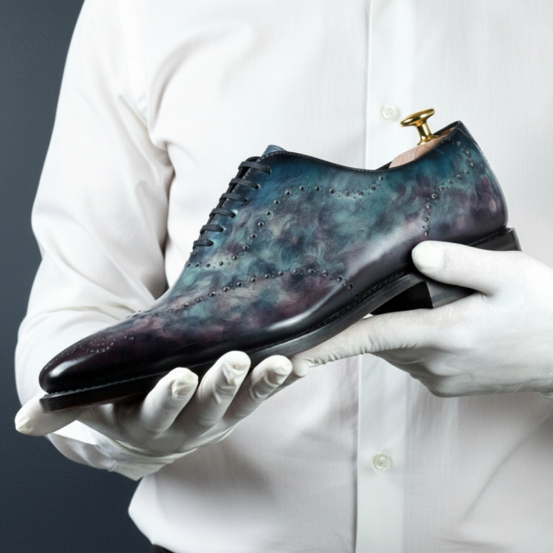 Person holding a pair of MERRIMIUM WHOLECUT shoes with gloves on a plain background