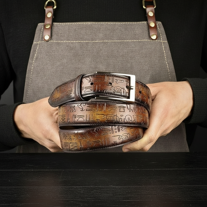 Person holding a brown MERRIMIUM leather belt with intricate designs against a dark background